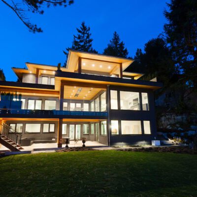A beautiful home at twilight with floor to ceiling windows on each of its three floors.