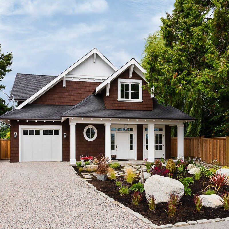 A cozy dark-stained wood-panelled home with fresh white trim sits behind a rock garden.