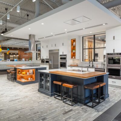 A staged modern kitchen in an appliance store featuring remodelled kitchen island, leather stools, and under cabinet lighting.