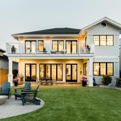 Grand, warmly lit backside of a lakeside home in Summerland, featuring numerous windows and timeless architectural charm.