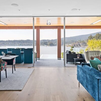 Open-concept dining and living area with floor-to-ceiling windows showcasing stunning lake views, in a custom craftsman-style home in Belcarra Bay.