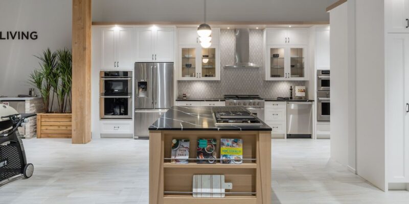 A large open concept white kitchen showroom featuring a marble top kitchen island.