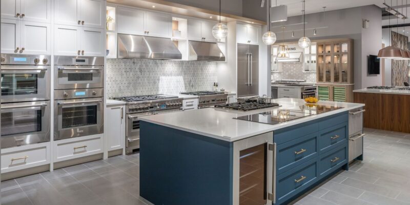 A renovated commercial kitchen with accent blue island, bright white cupboards and added lighting.