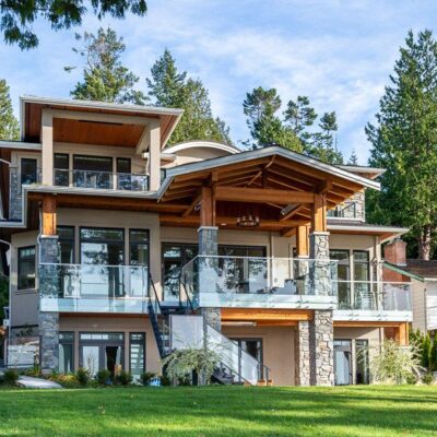 Front exterior of a West Coast traditional ocean bluff home, featuring stone accents, pillars, and multiple balconies designed to capture the view.