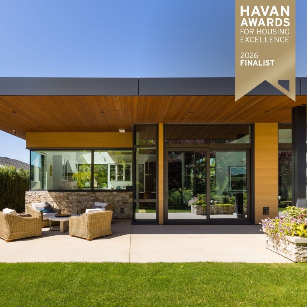 Modern custom home with a covered outdoor patio featuring wood soffits, black columns, large glass doors, and landscaped garden, labeled as a 2026 HAVAN Awards finalist for housing excellence.